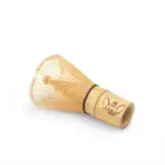 Bamboo matcha whisk lying on its side with fine looped tines and a Moba Matcha logo on the handle