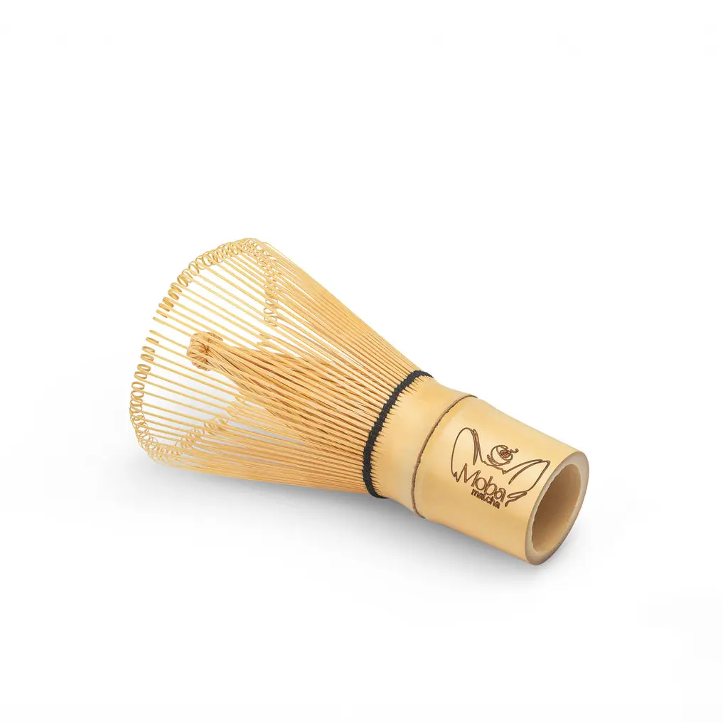 Bamboo matcha whisk lying on its side with fine looped tines and a Moba Matcha logo on the handle