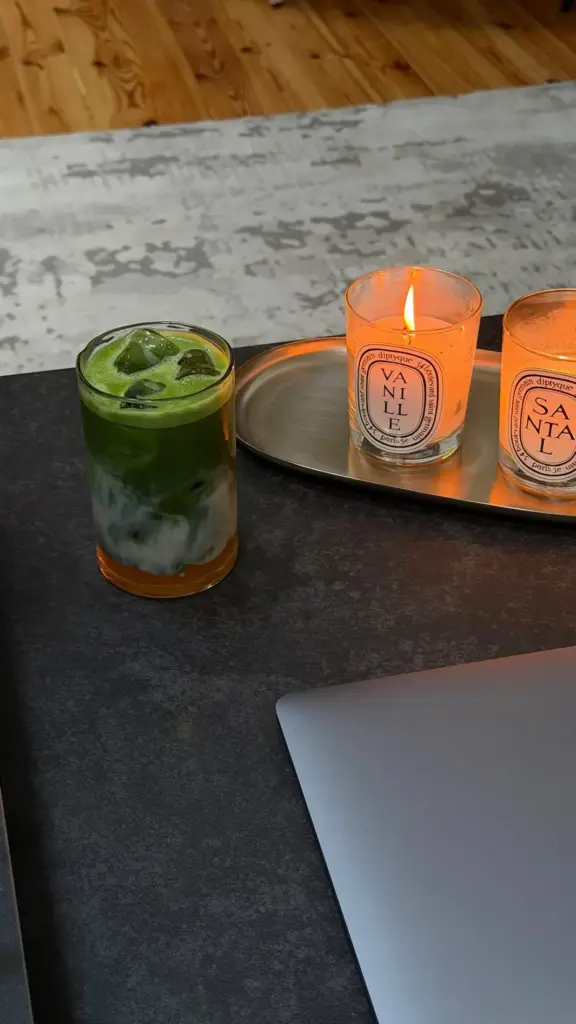 Iced green matcha drink beside two glowing candles on a dark table