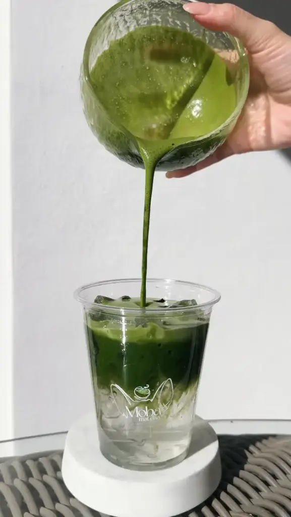 Thick green matcha poured from a glass bowl into an iced Moba Matcha cup