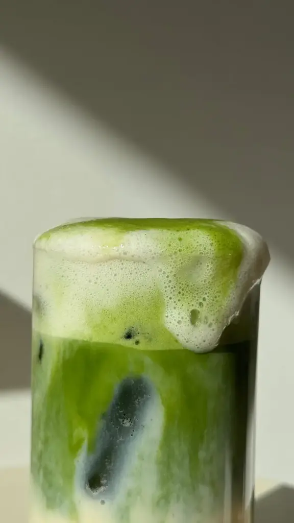 Close-up of a green iced drink topped with thick pale foam in a clear glass