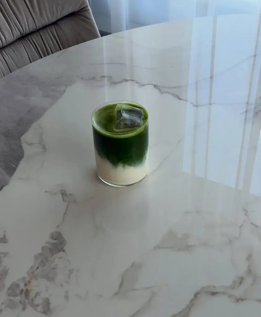 Layered green and white iced drink in a clear glass on a marble-patterned table