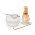 Glass matcha bowl with metal sifter, bamboo whisk on a holder, and bamboo scoop