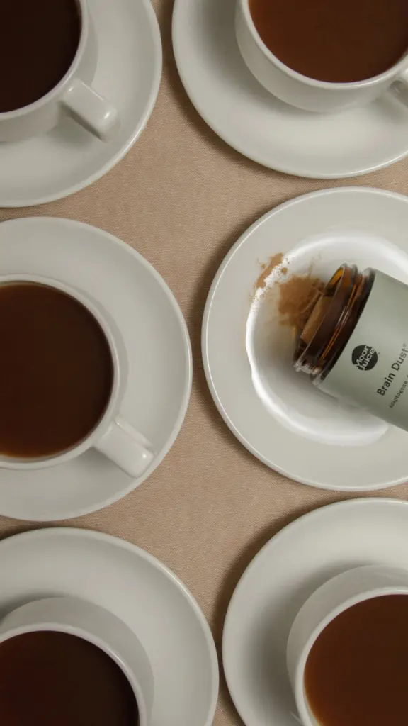 Moon Juice Brain Dust bottle beside white cups filled with brown drinks
