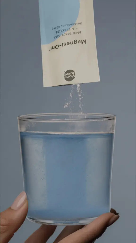 Magnesi-Om packet pouring powder into a glass of blue water held by hands