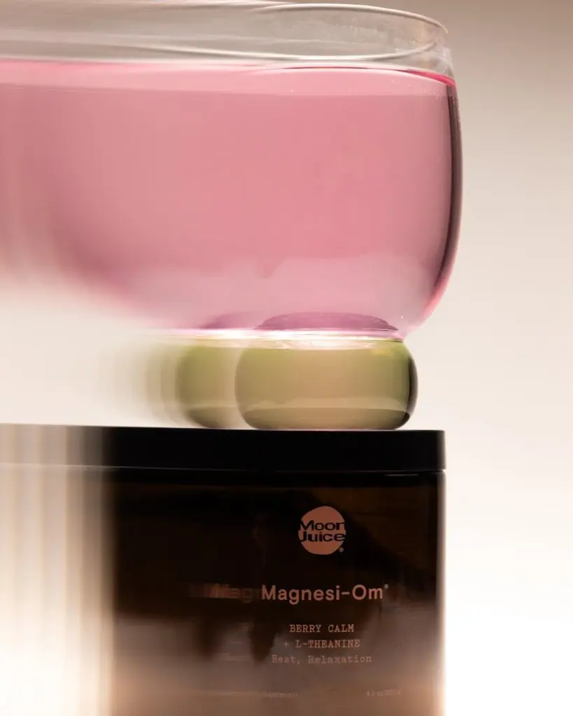 Pink drink in a clear glass balanced on a Moon Juice Magnesi-Om jar