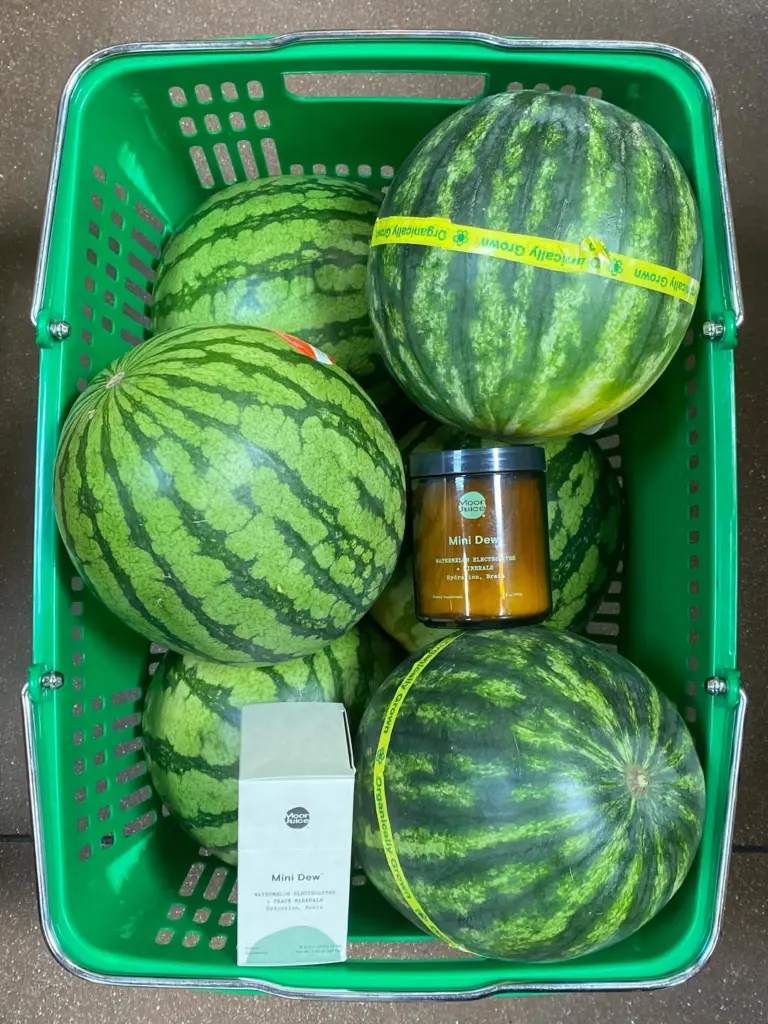 Moon Juice Mini Dew jar and box surrounded by watermelons in a green basket