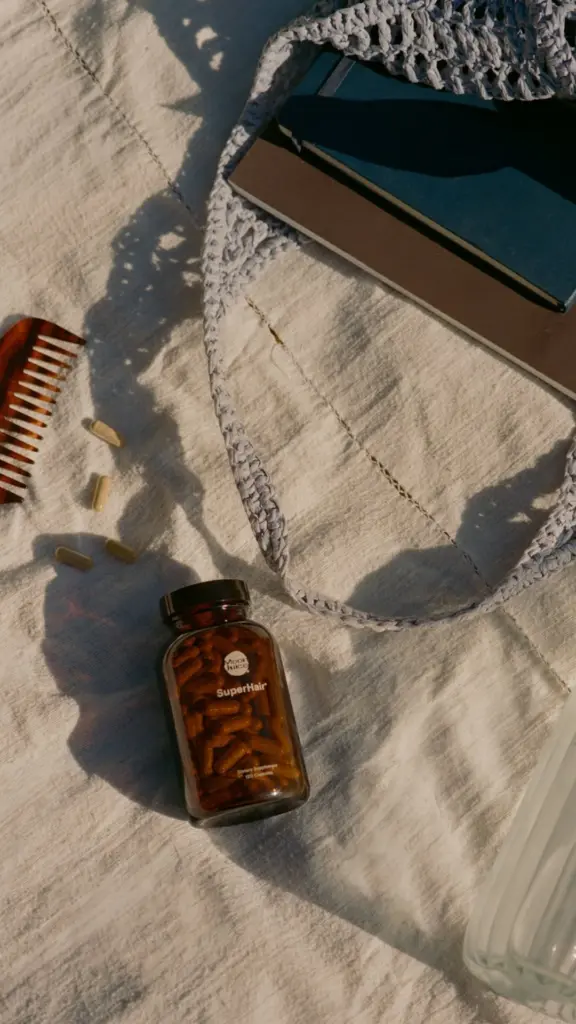 SuperHair bottle and loose capsules beside a comb, bag, and notebooks