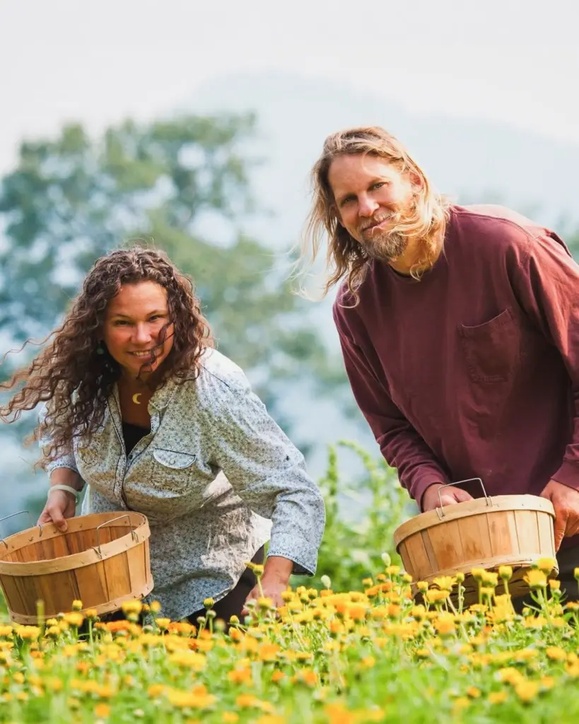 Two adults holding wooden baskets in a field of yellow flowers