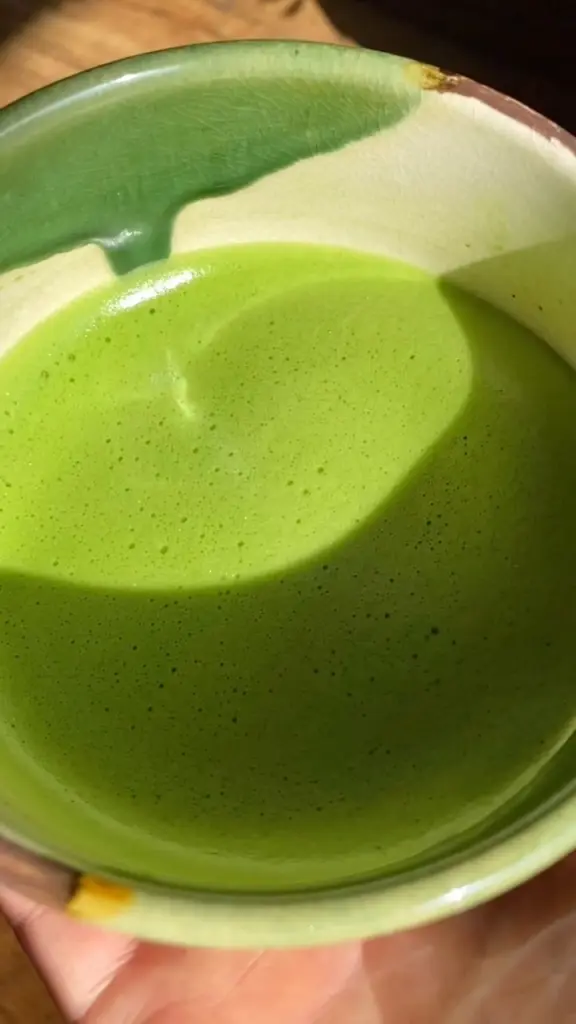 Bowl of vivid green matcha crossed by strong sunlight and shadow
