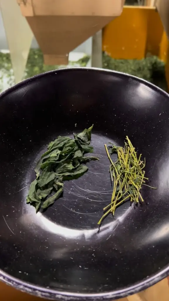 Two small piles of dried tea leaves and stems in a black bowl