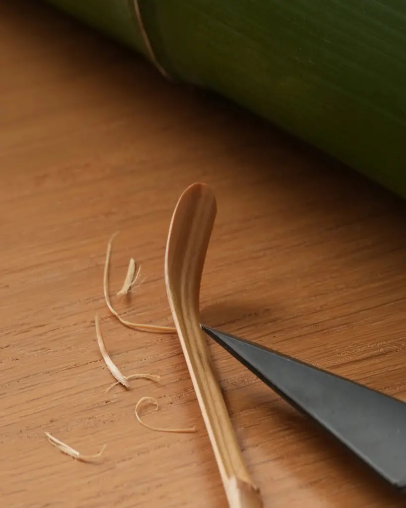 Bamboo tea scoop being shaped with a carving knife on a wooden surface