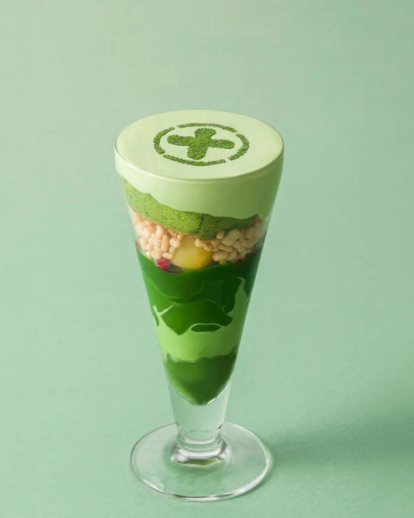 Tall green parfait with cream, crisp pieces, fruit, and a powdered emblem