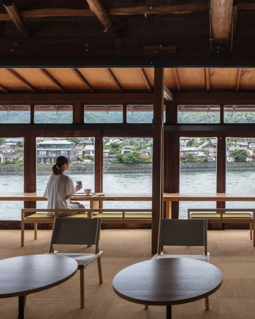 Guest holding a cup at a wooden counter overlooking a river