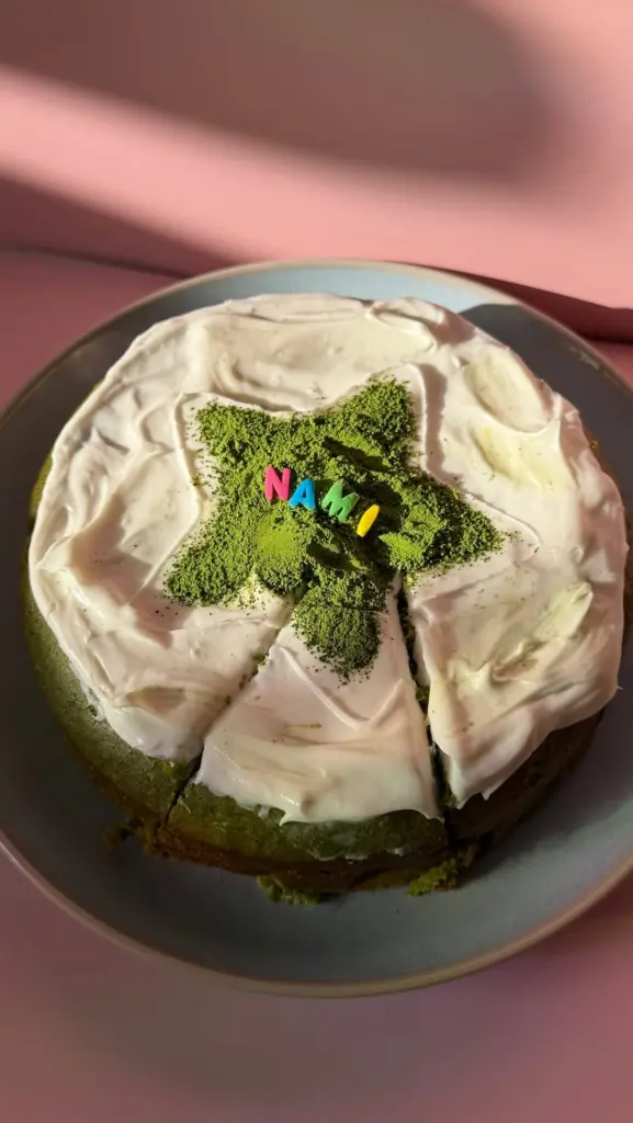 Round green cake with white frosting, matcha powder, and colorful Nami letters