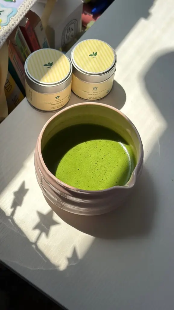 Bright green matcha in a pink ceramic bowl beside two tins