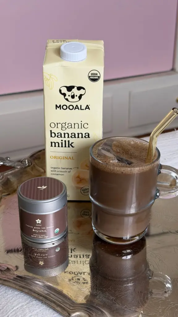 Nami hojicha tin beside a glass mug of iced brown drink and a banana milk carton