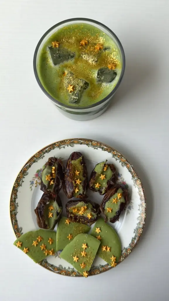 Iced green drink beside a plate of dates and green treats with gold stars