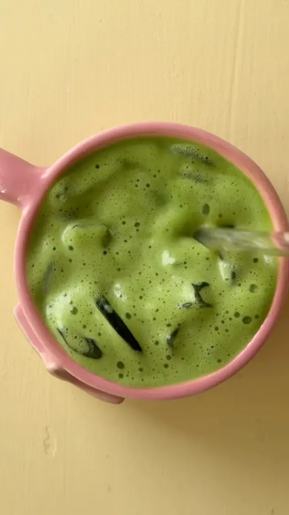 Foamy iced matcha being stirred in a pink mug