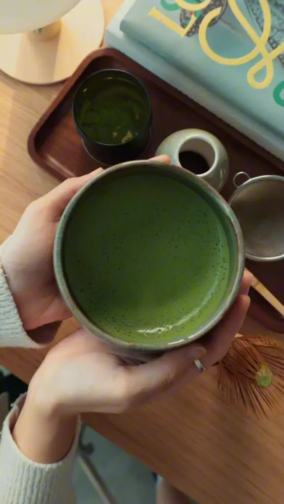 Hands holding a ceramic bowl of frothy green matcha