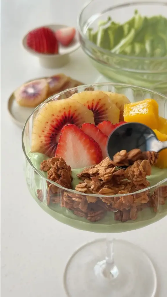 Green yogurt parfait topped with granola, strawberries, kiwi, and mango