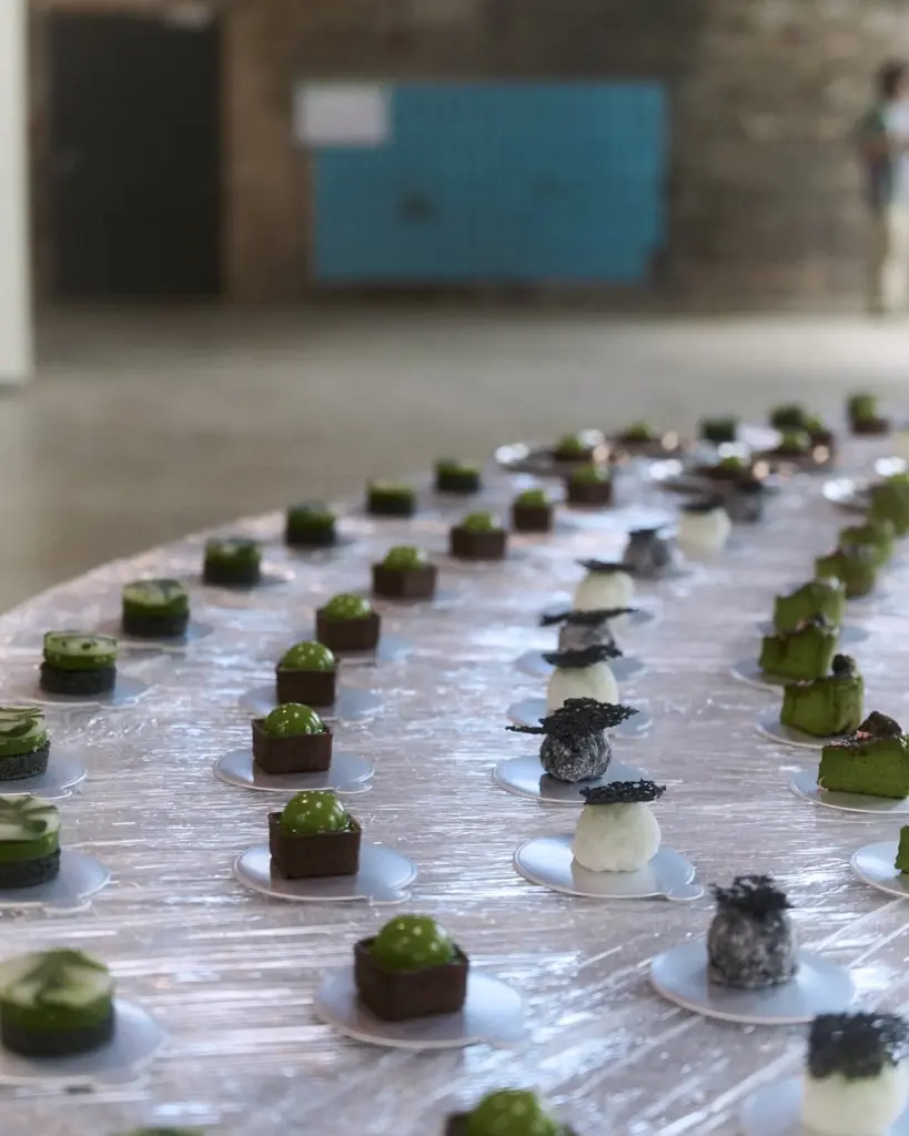 Rows of small green, white, and dark desserts on individual plates
