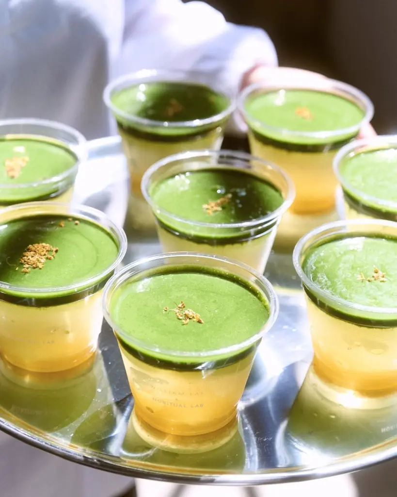 Clear cups of golden drinks topped with smooth green layers on a metal tray