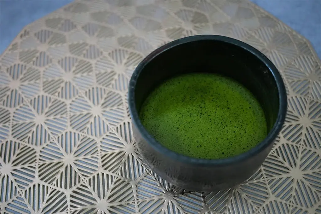 Dark bowl filled with frothy green matcha on a geometric pattern