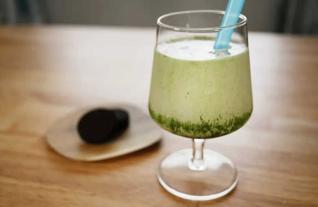 Frothy green drink in a stemmed glass with a blue straw