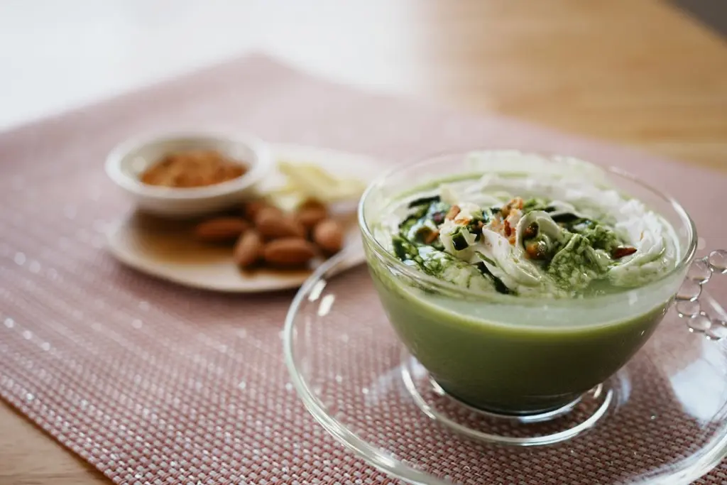 Green matcha dessert topped with white cream, green drizzle, and chopped nuts