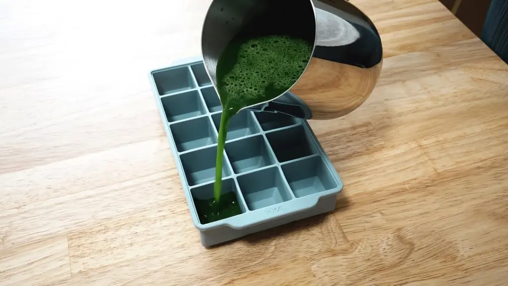Green matcha liquid poured from a metal pitcher into an ice cube tray