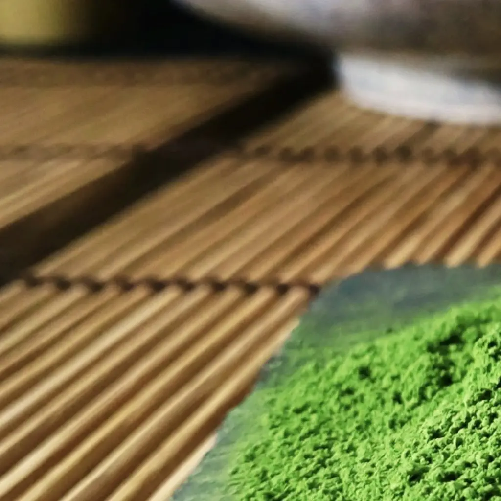Bright green matcha powder beside a bamboo whisk