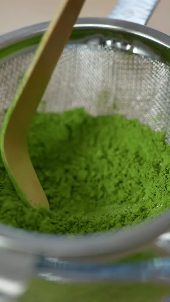 Bright green matcha powder in a fine mesh sieve with a wooden utensil