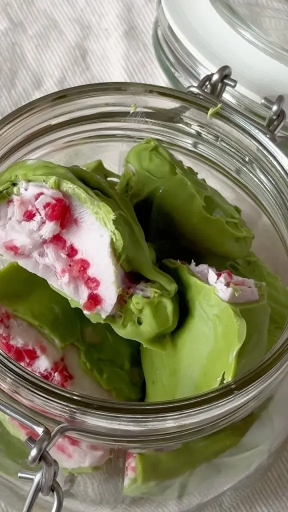 Green-coated confections with white and red centers in an open glass jar