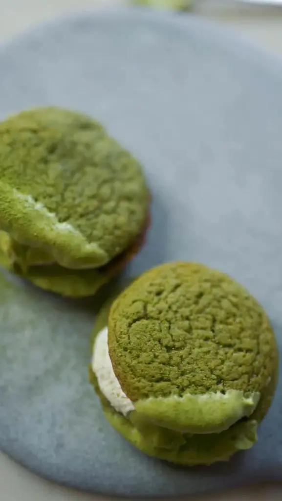 Two green sandwich cookies with pale and green fillings on a dark plate