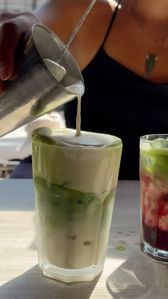 Foam being poured onto a green iced drink in a tall glass
