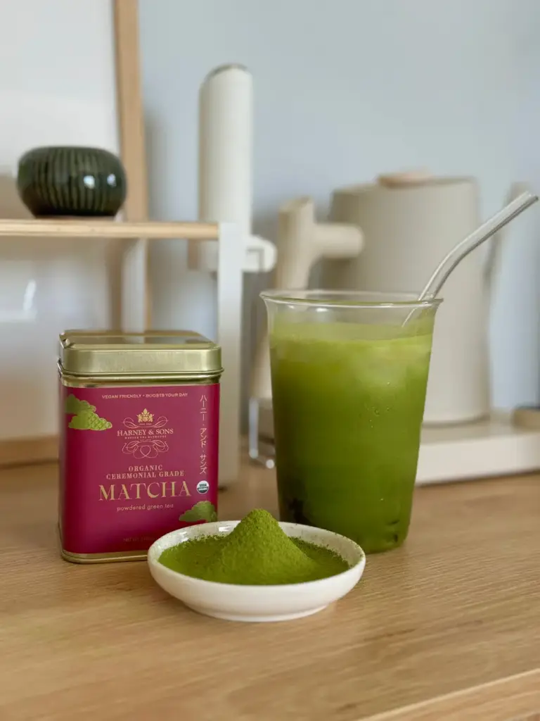 Harney & Sons Organic Ceremonial Grade Matcha tin beside a glass of iced matcha and a dish of green powder