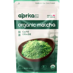 Front of an Aprika Life organic café-grade matcha pouch with a bowl of green matcha powder