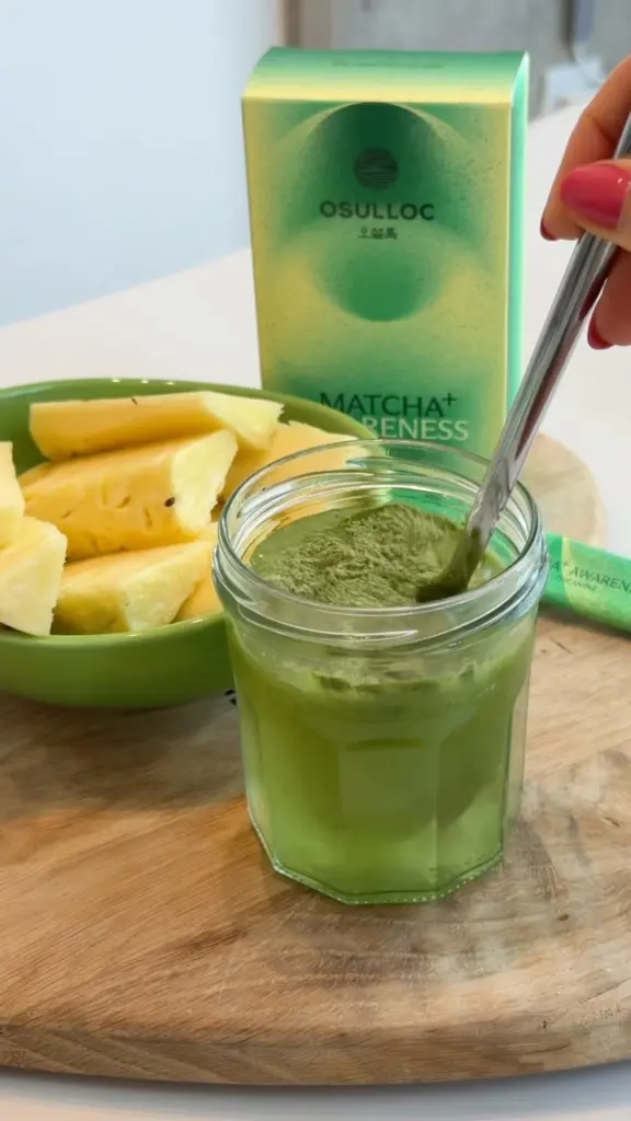 Green drink being stirred beside pineapple pieces and O'sulloc packaging