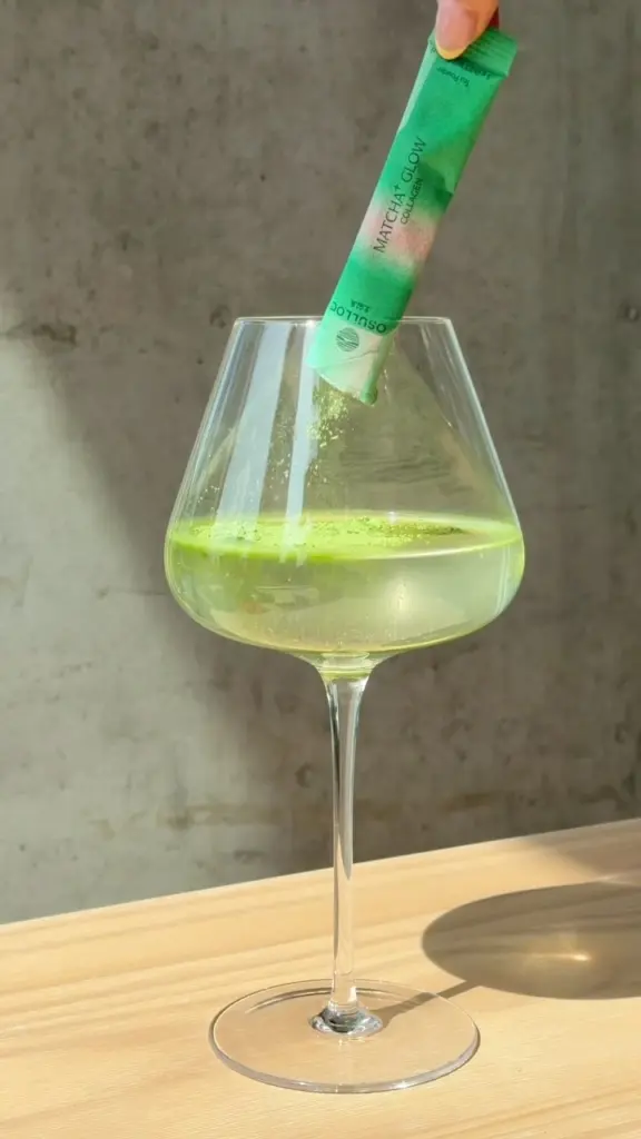 Green powder poured from an O'sulloc packet into a stemmed glass of water