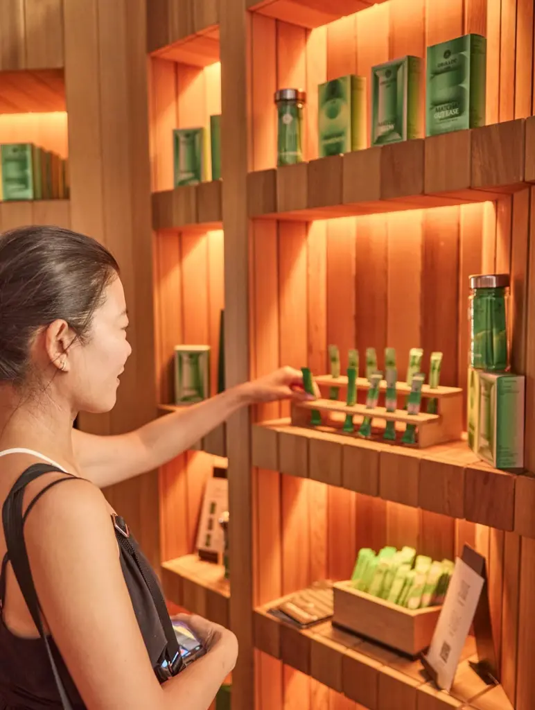 Woman reaching toward green packets on a warmly lit wooden display