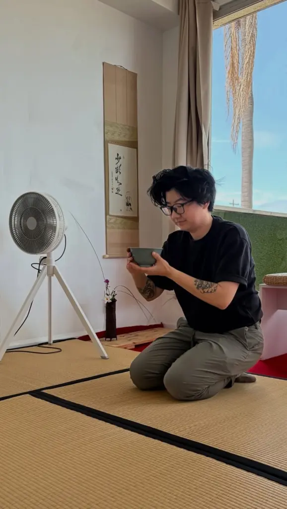 Person kneeling on tatami mats while holding a green tea bowl