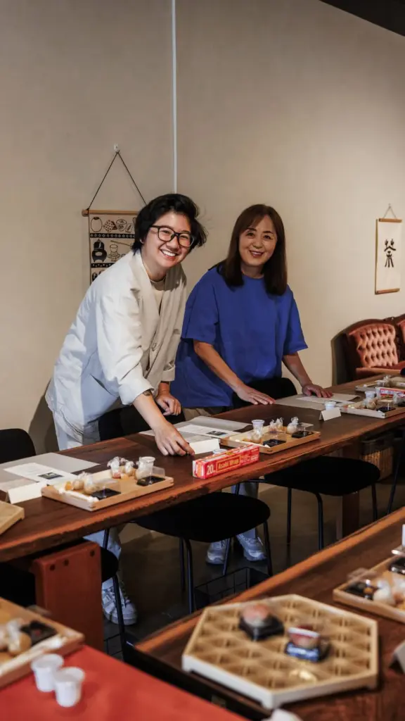 Two smiling people standing behind a long table set with small dishes