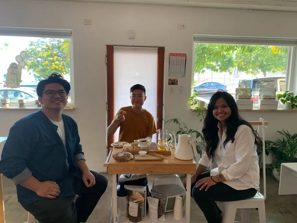 Three smiling people seated around a small table with tea ware