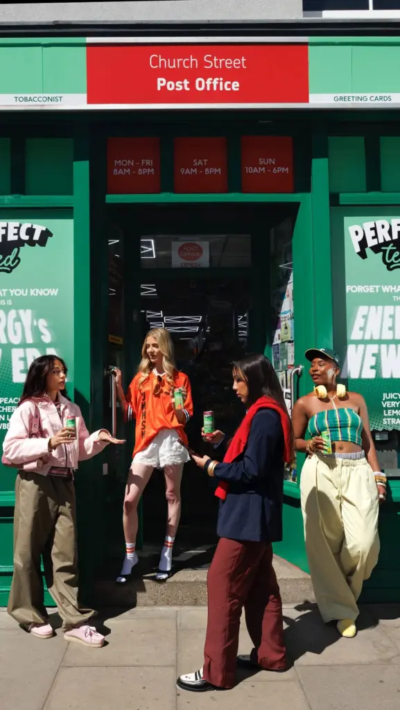 Four women holding PerfectTed cans outside the green Church Street Post Office