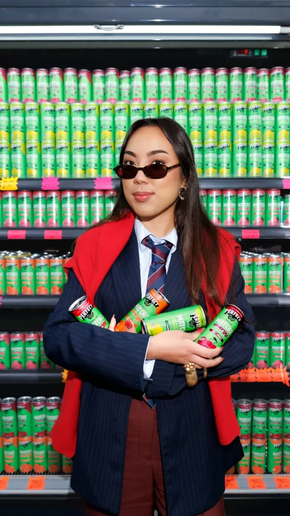 Person holding four PerfectTed matcha cans in front of shelves filled with colorful cans