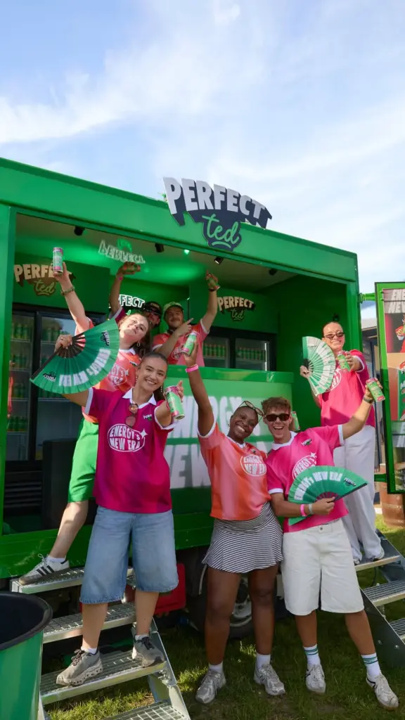 Group in colorful shirts holding PerfectTed cans and fans outside a green stand