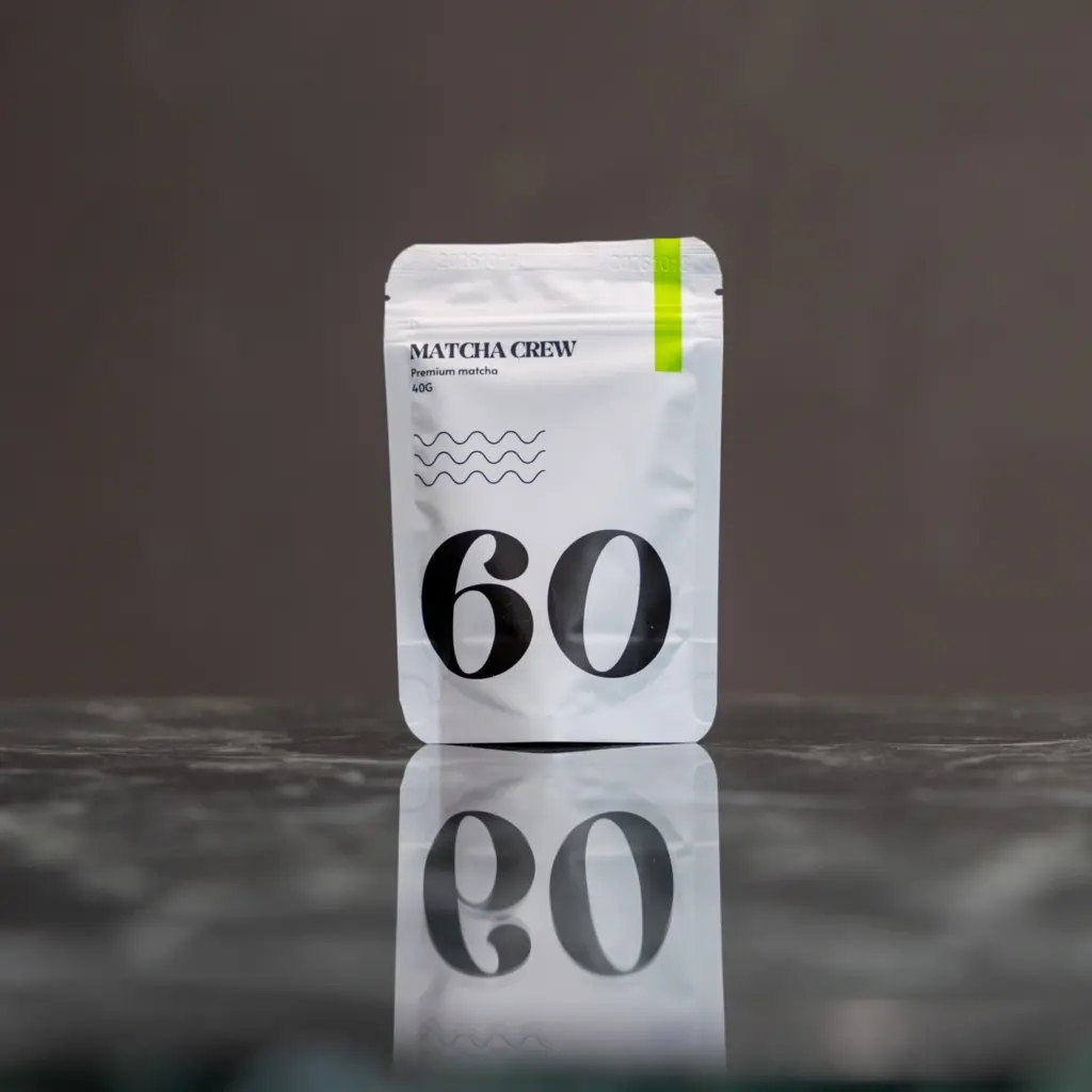 Matcha Crew No. 60 premium matcha pouch on a dark reflective surface