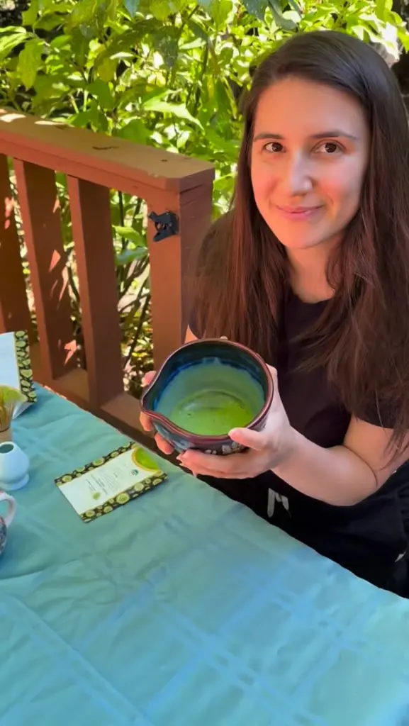 Woman holding a ceramic bowl of bright green matcha at an outdoor table