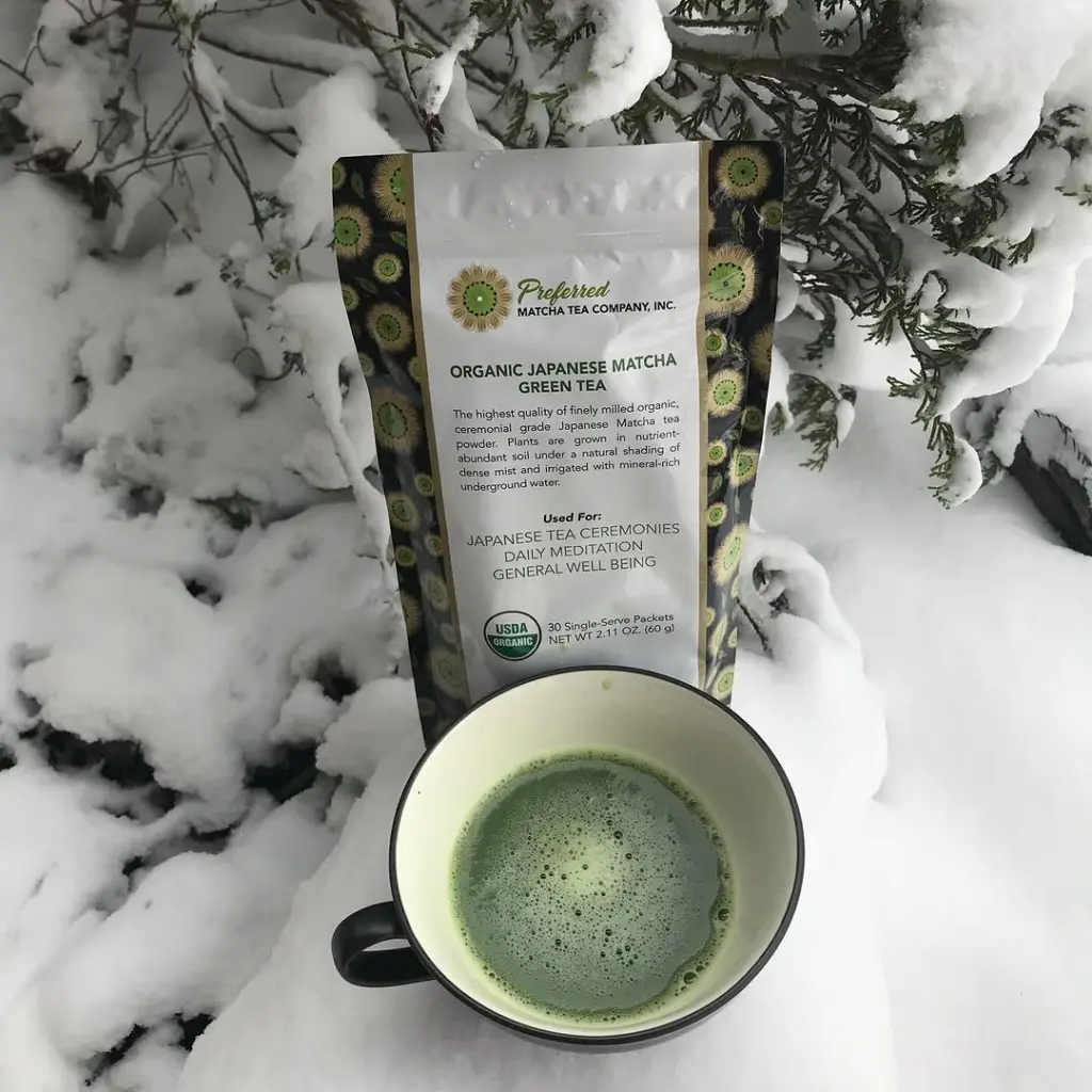 Cup of frothy green matcha beside a Preferred matcha package in snow